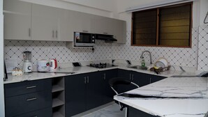 Een kleine keuken met witte kastjes, een magnetron, een gasfornuis en een spoelbak.