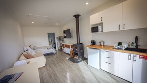 Ein kompaktes Hotelzimmer mit Küchenzeile, einem Bett, einer kleinen Sitzecke und einem an der Wand befestigten Fernseher.
