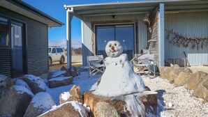 Ein Schneemann vor einem Gebäude mit Garage, einem abgestellten Geländewagen und einer Holzhütte mit Geweihen.