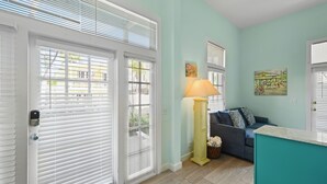 A living room with a teal wall, a blue sofa, a yellow floor lamp, and a painting of a market scene.