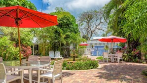 A patio with round tables and chairs, red umbrellas, and a pool area. - Old Town Key West suite w/ pool & pet-friendly (Key West)