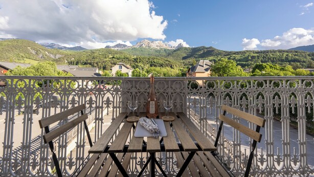 A balcony with a table set for two, a bottle of wine, and a cutting board. - Grande Anita - City center - Private parking (Barcelonnette)