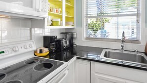 A modern kitchen with white cabinets, a black countertop, a stainless steel sink, and a window with blinds.