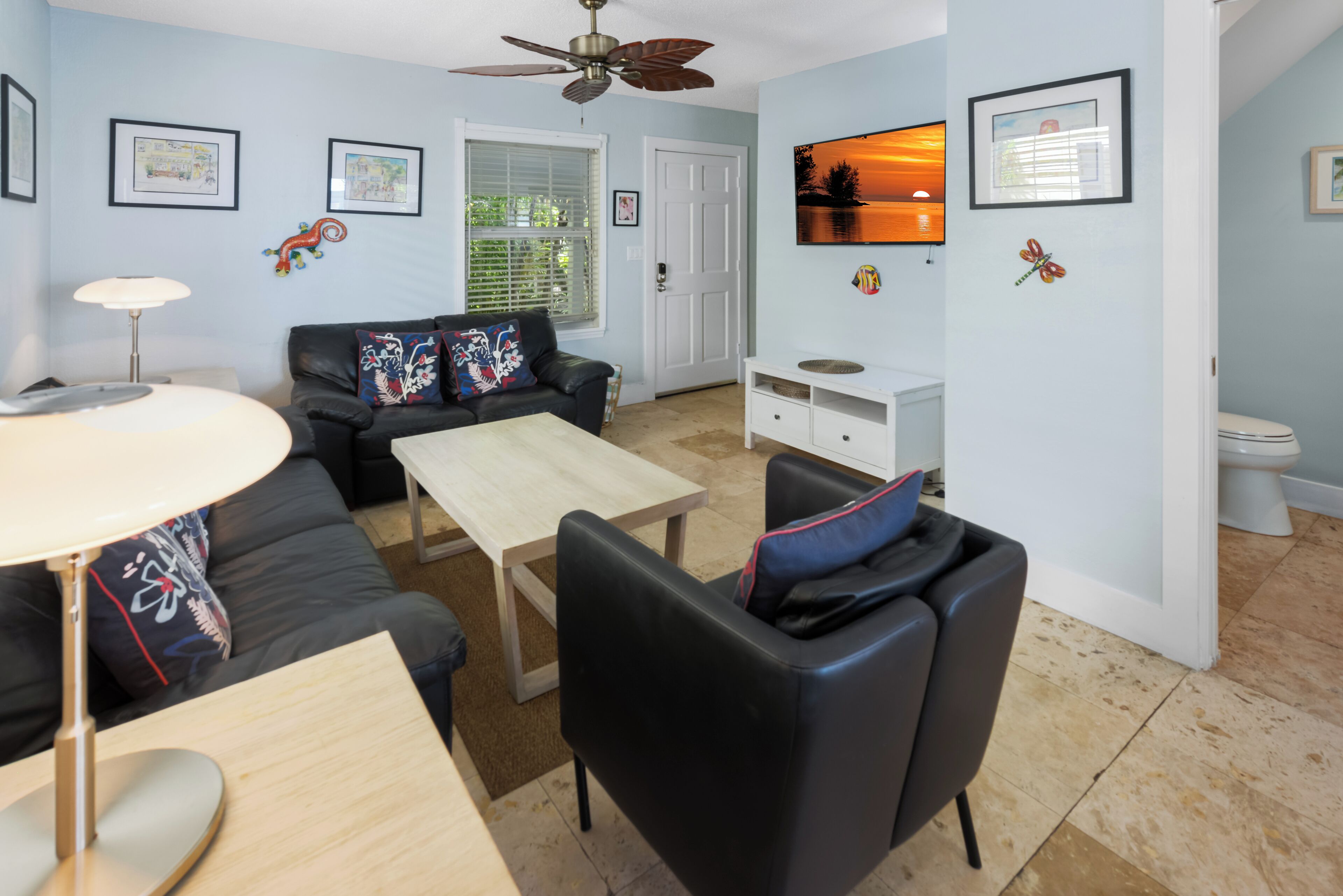 A living room with a ceiling fan, a sofa, a coffee table, and a TV mounted on the wall.