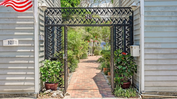 A gated entrance with a number sign, a brick pathway, and potted plants.