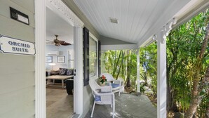A covered porch with white wicker furniture, a ceiling fan, and a sign reading "Orchid Suite."