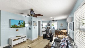 A living room with a sofa, a coffee table, a TV mounted on the wall, and a ceiling fan.