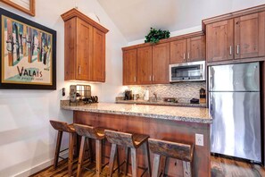 Una cocina con armarios de madera, un refrigerador de acero inoxidable, un microondas y una zona de bar con taburetes.