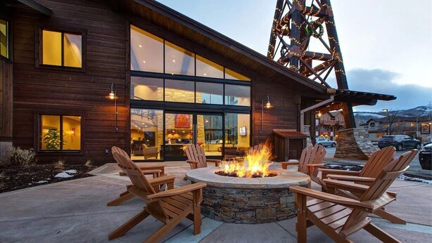 A wooden building with large windows and a fire pit with chairs.