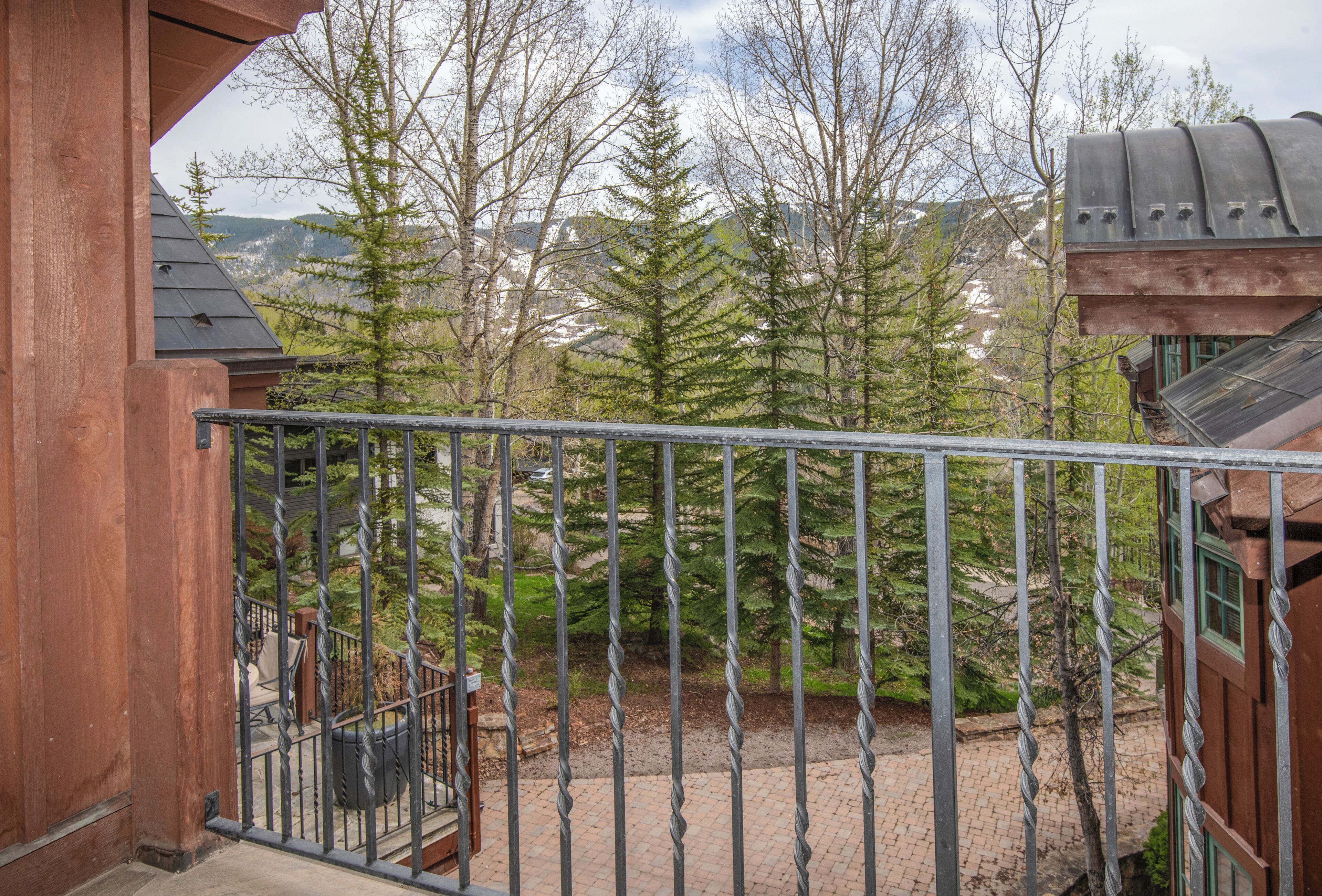 Un balcon doté d’une balustrade en métal, donnant sur une zone boisée et des montagnes.