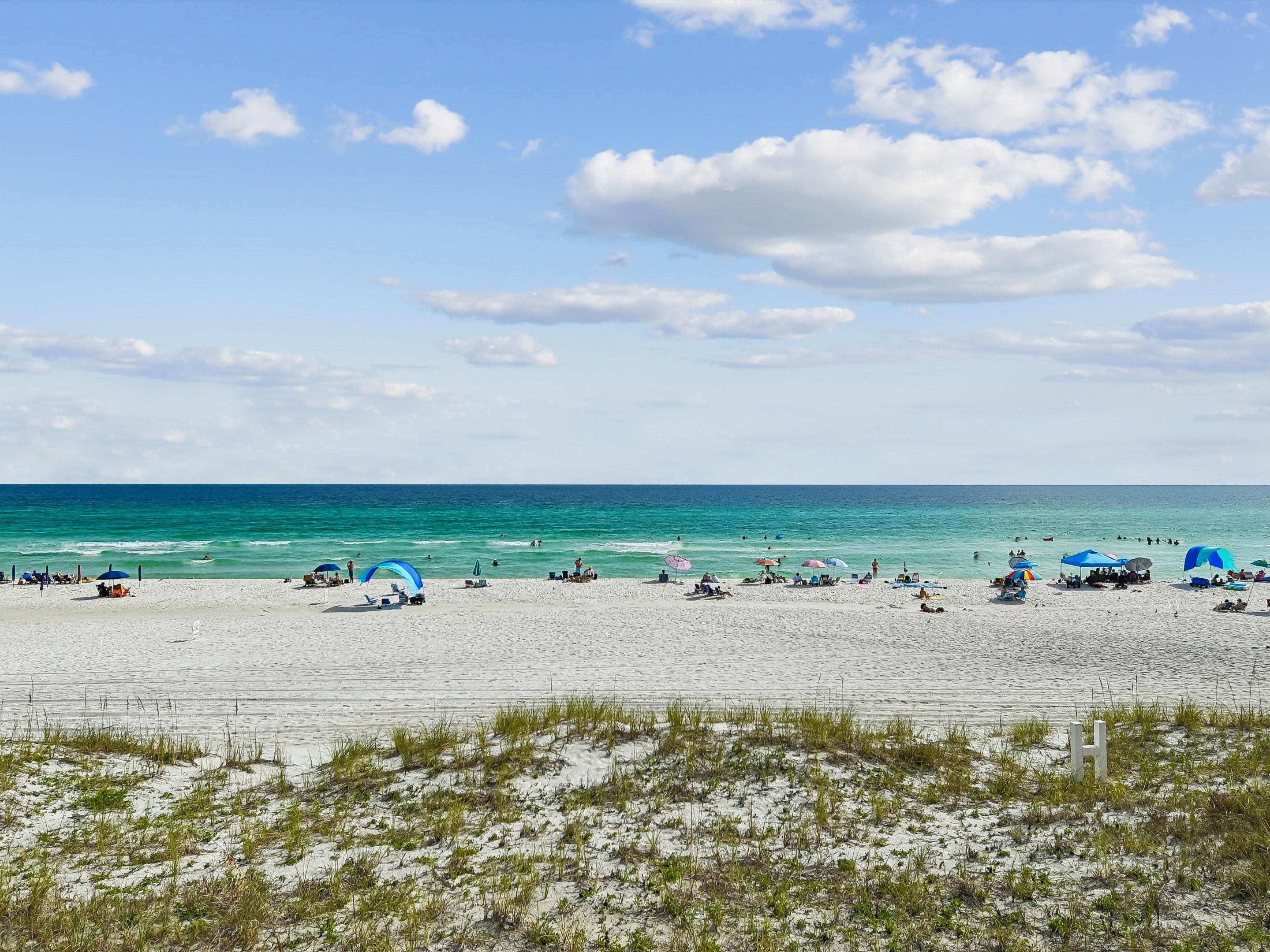 Een strand met wit zand, helderblauw water en enkele parasols.