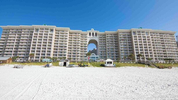 Un grand hôtel doté de nombreux balcons, d’une entrée en arc de cercle et d’une plage de sable devant.
