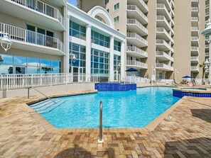 A swimming pool with a tiled edge, surrounded by a brick deck with numbered lounge chairs.
