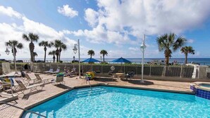 A swimming pool with clear blue water, surrounded by lounge chairs and umbrellas, with palm trees and a view of the ocean in the background. - Majestic Sun #412A | Beach Views & Fun On-Site Amenities! (Miramar Beach)