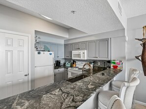 A kitchen with white cabinets, a granite countertop, a stainless steel sink, and a microwave.