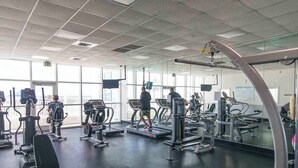 Une salle de sport équipée de divers appareils d ’exercice, dotée de grandes fenêtres et d’un mur entièrement recouvert de miroirs.