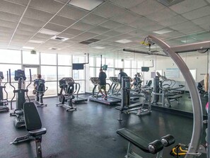 A gym with various exercise machines, large windows, and a mirrored wall. - Majestic Sun #412A | Beach Views & Fun On-Site Amenities! (Miramar Beach)