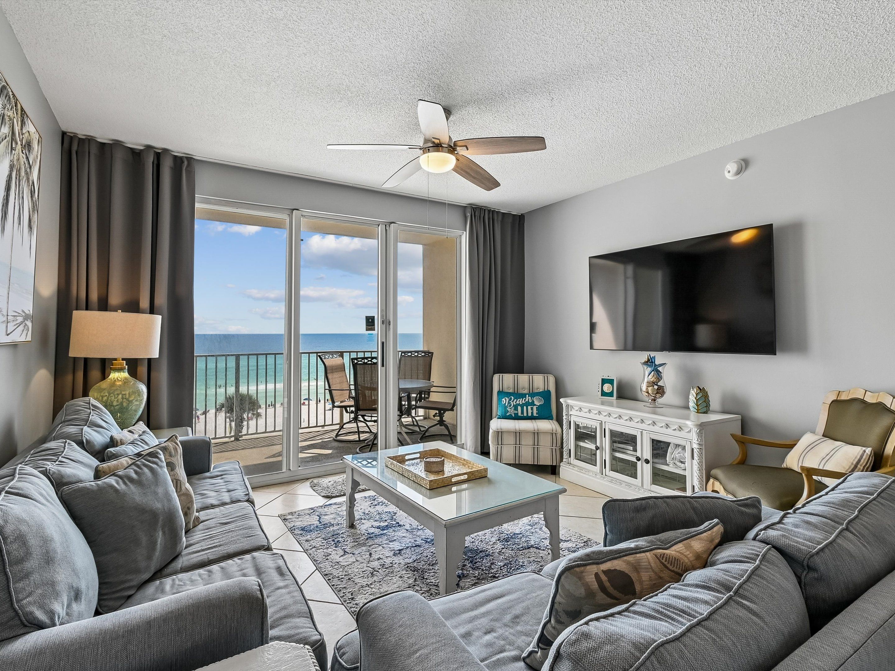 A modern living room with a balcony, a flat-screen TV, and a ceiling fan.