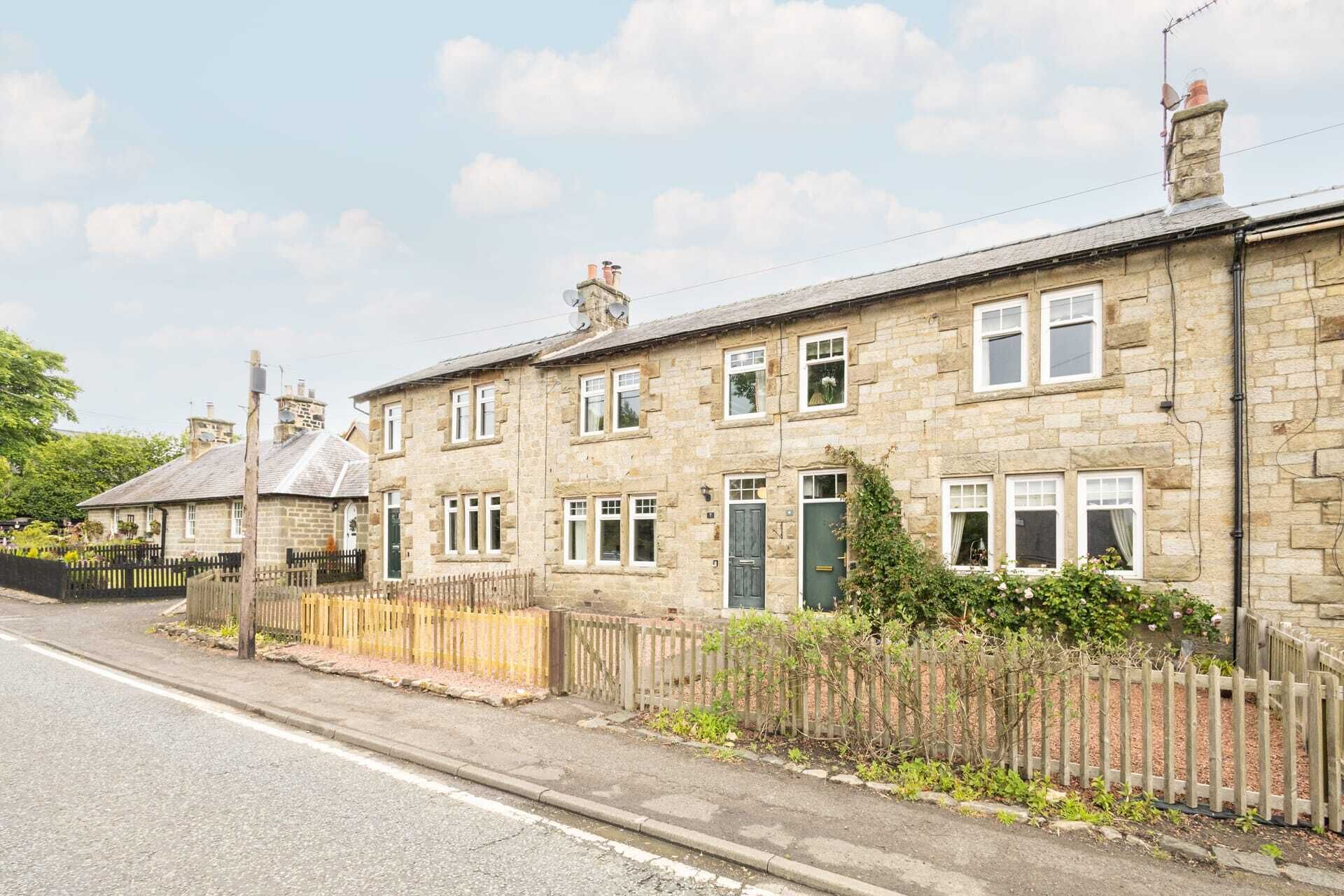 A row of stone houses with uniform architecture, a clear road in front, and a wooden fence along the side.
