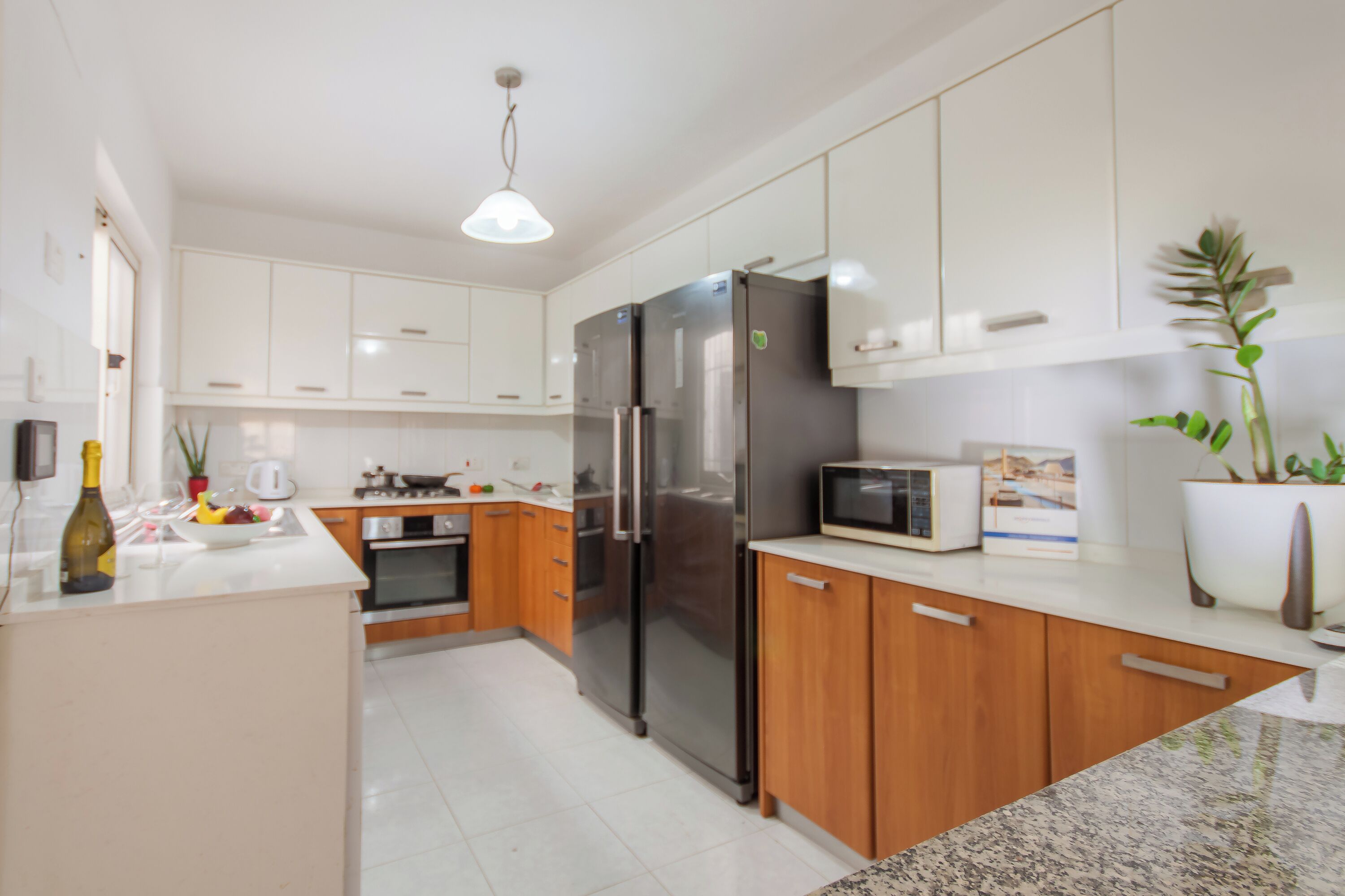 Una cocina moderna con armarios blancos, un refrigerador de acero inoxidable, un microondas y una encimera de granito.
