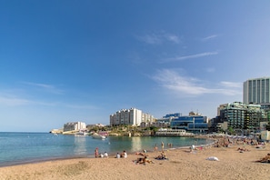 A beach with people, a boat, and buildings in the background.