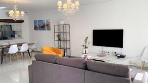Una sala de estar moderna con sofá, mesa de comedor, sillas, televisor y candelabro.