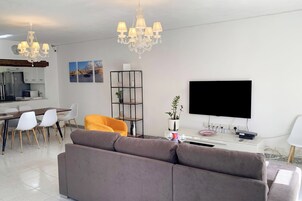 A modern living room with a sofa, dining table, chairs, a TV, and a chandelier.