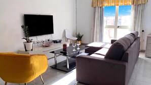Una sala de estar moderna con televisor de pantalla plana, un sofá, un sillón amarillo, una mesa de centro y una mesa de comedor.