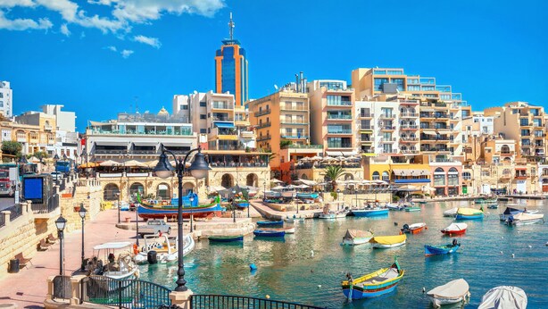 Un paisaje urbano costero con un puerto deportivo, edificios y una torre destacada.
