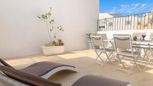 A sunlit outdoor seating area with lounge chairs and a table, surrounded by a low wall and a railing. - SwieqiStay room5 shared bath - Paceville (Swieqi)