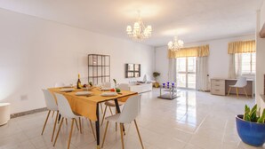 Un comedor amplio con una mesa de madera, sillas blancas y una lámpara de araña.