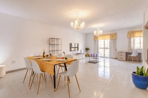 A spacious dining area with a wooden table, white chairs, and a chandelier.