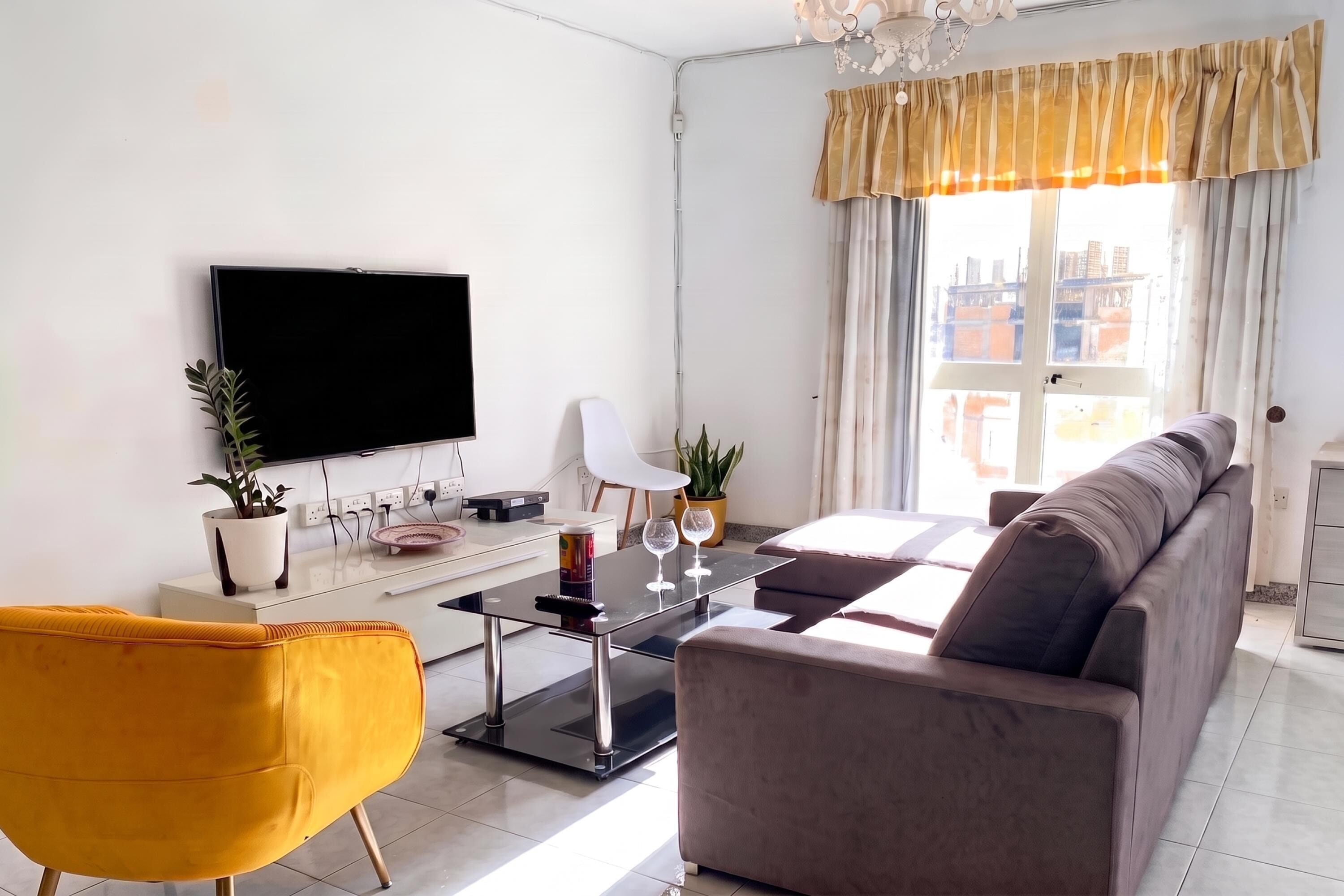 A modern living room with a flat-screen TV, a sofa, a coffee table, and a yellow chair.