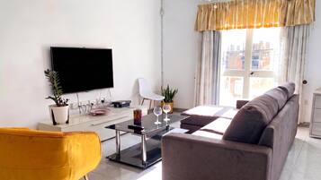 A modern living room with a flat-screen TV, a sofa, a coffee table, and a yellow chair.