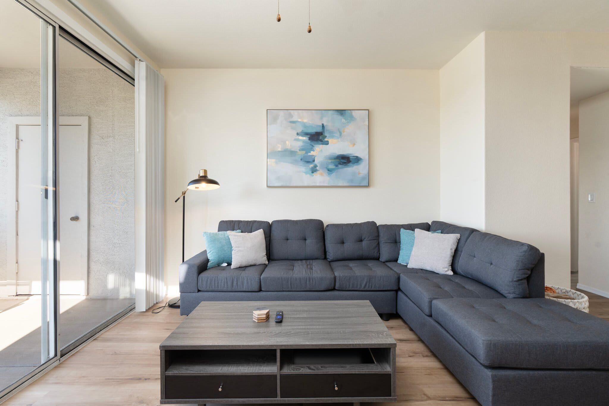 A modern living room with a sectional sofa, a coffee table, and a large abstract painting on the wall.