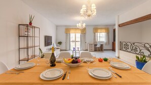 Comedor con una mesa preparada para cuatro, una araña y vista al salón.