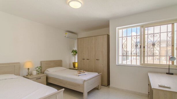 Un dormitorio con dos camas, un escritorio, un armario y una ventana con rejas.