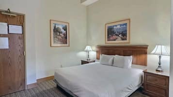 A hotel room with a large bed, two bedside tables with lamps, a wooden door, and two framed landscape paintings on the walls.
