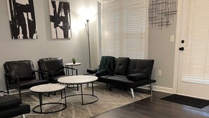 A modern living room with dark wood flooring, a black leather sofa, two white round tables, and abstract art on the walls. - Charming 2-bedroom townhome in wonderful Raleigh with WiFi, AC (Raleigh)
