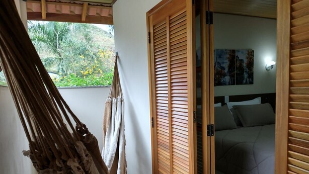 Eine Hängematte, Holztüren, ein Bett mit Kopfteil und Blick auf grüne Natur.