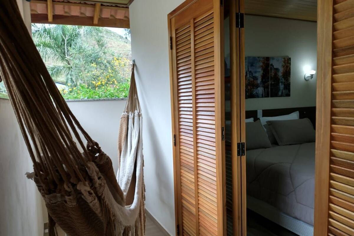 A hammock, wooden sliding doors, and a bed with a headboard in a room with a view of greenery outside.
