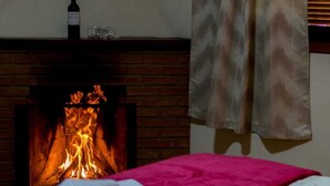 Ein Zimmer mit Kamin aus Backsteinen, einer Weinflasche auf dem Sims und einer rosa Decke auf dem Bett.