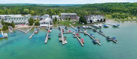 A marina with boats docked, a hotel with multiple buildings, and a forested landscape in the background.