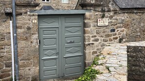 A stone building with a grey double door, a small window, and a sign indicating 'Marches de Porte d'Bas.'