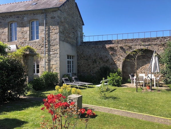 A stone building with a garden, outdoor seating, and a stone bridge.