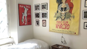 A room with two single beds, a radiator, a desk with a lamp, and a large movie poster on the wall.