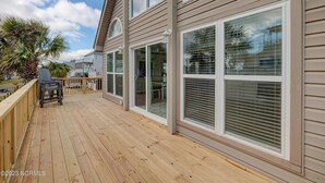 Une terrasse en bois avec un barbecue et des chaises, de grandes fenêtres et une vue sur le ciel.