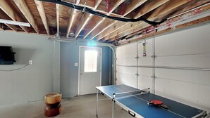 Una habitación con mesa de ping pong, un barril de madera y una puerta con ventanal.