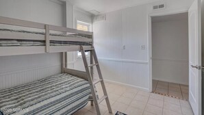 Una habitación con literas, una escalera, una ventana y una puerta que da a otra habitación.