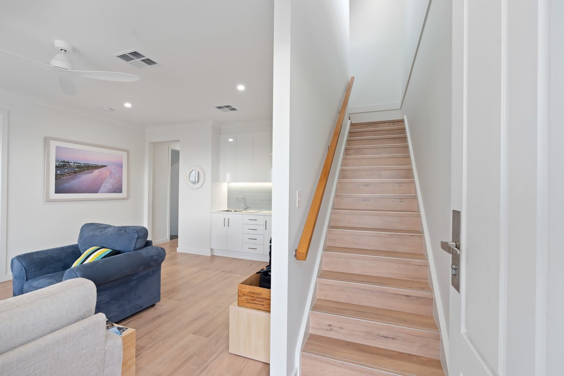 Una sala de estar moderna con un sofá azul, una escalera de madera y una zona de cocina.